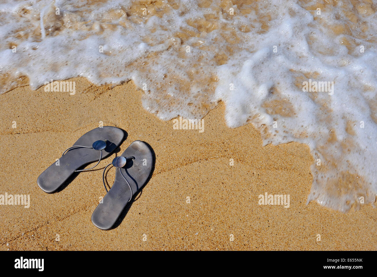 Flip-flop su una spiaggia a bordo dell'acqua Foto Stock