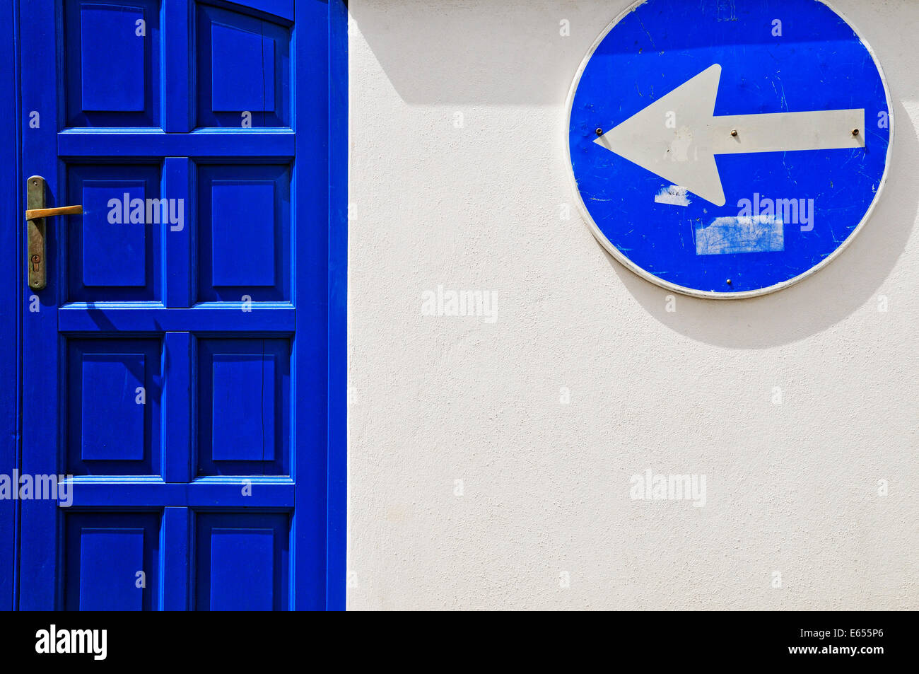 Strada segno di freccia e porta blu sul muro bianco Foto Stock