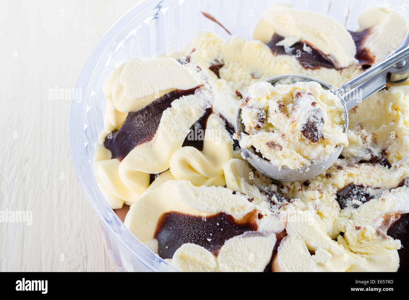 La vaniglia con gelato al cioccolato scoop raccolto fuori di un contenitore sul bianco sullo sfondo di legno Foto Stock