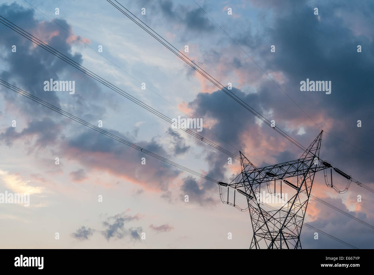 Silhouette di linee elettriche ad alta tensione e la torre contro una tempesta cielo nuvoloso al tramonto. Foto Stock