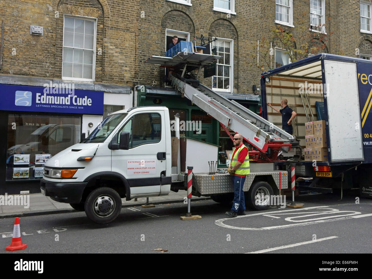 Traslochi uomini tramite ascensore per sollevare possedimenti al primo piano finestra, Londra Foto Stock