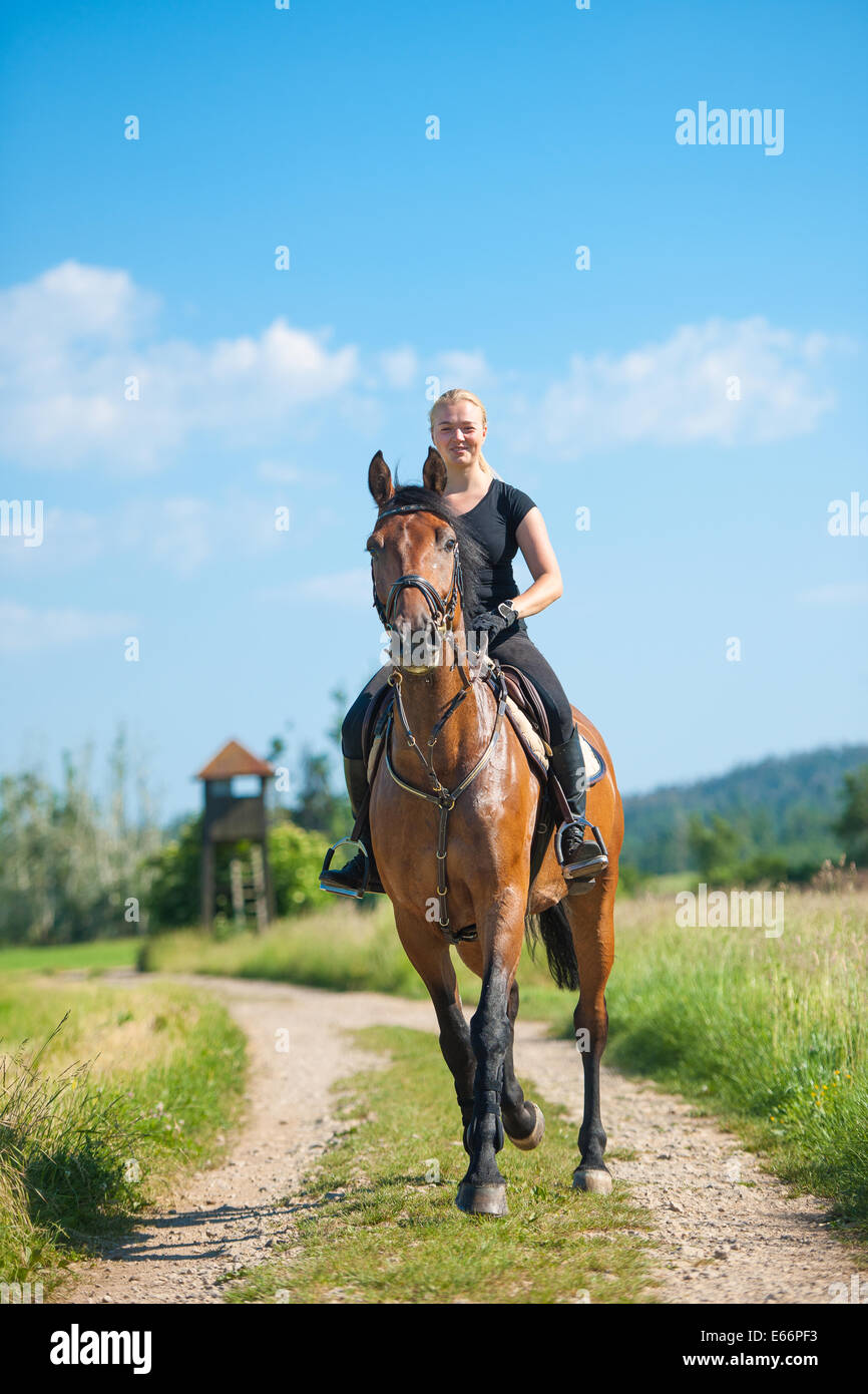 Giovane e bella donna bionda in sella ad un cavallo in un agriturismo Foto Stock