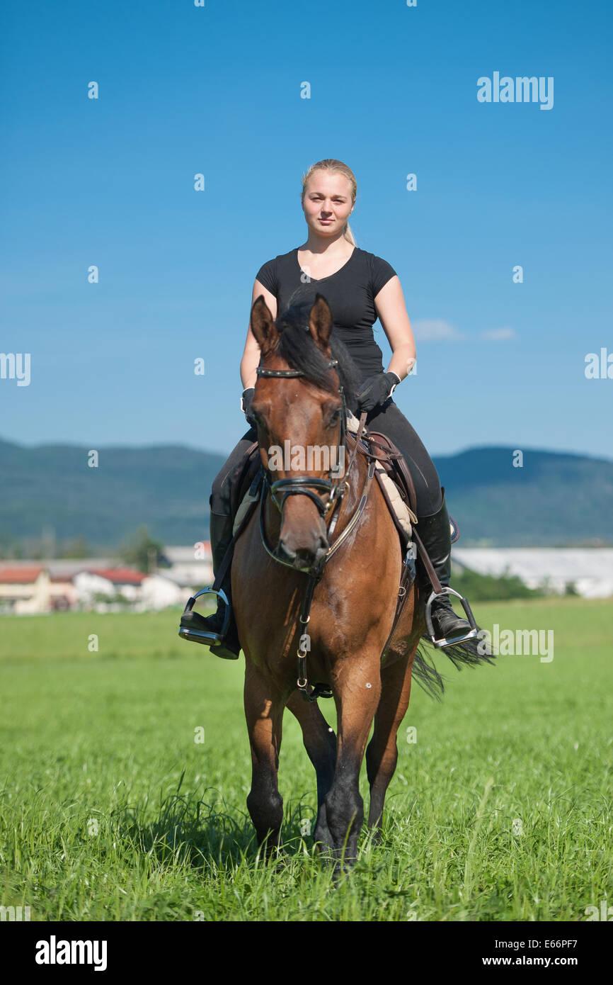 Giovane e bella donna bionda in sella ad un cavallo in un agriturismo Foto Stock