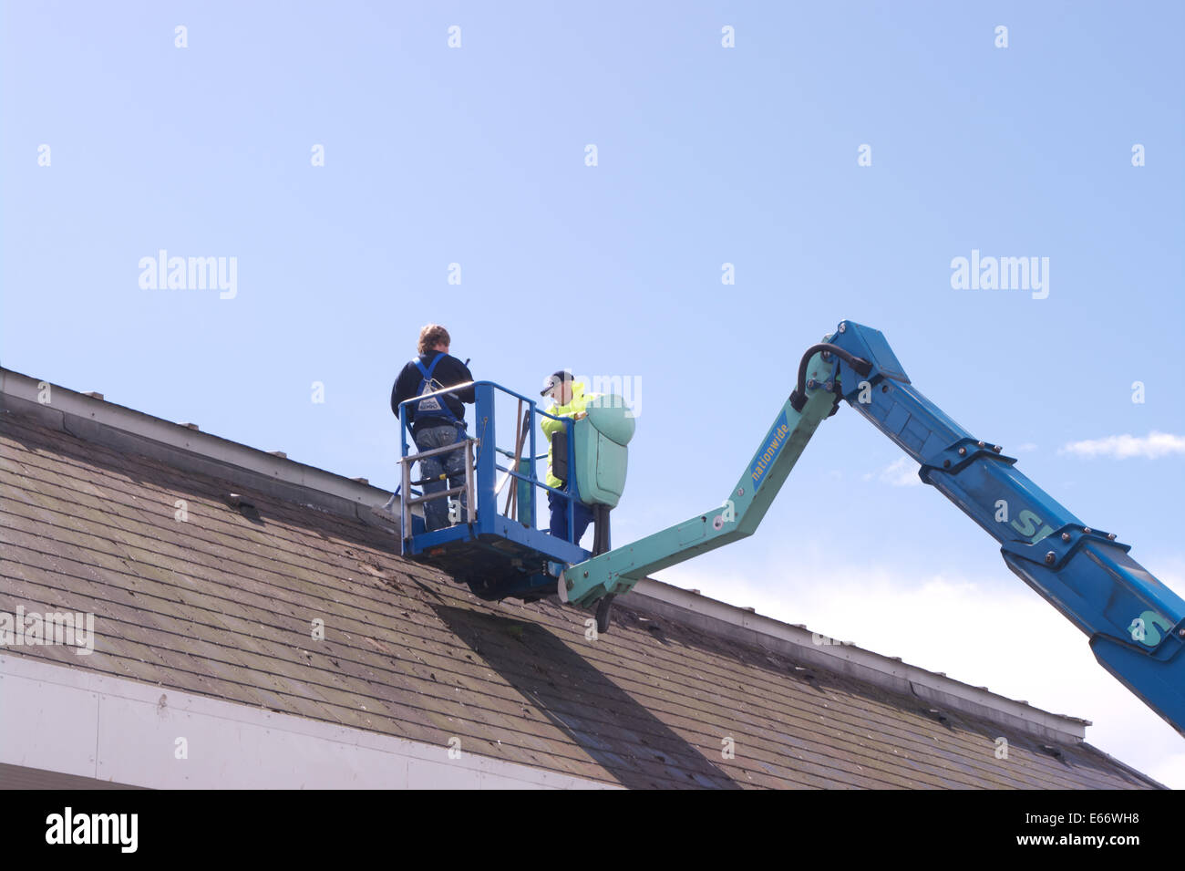 Due uomini al lavoro su un tetto da una piattaforma di accesso Foto Stock