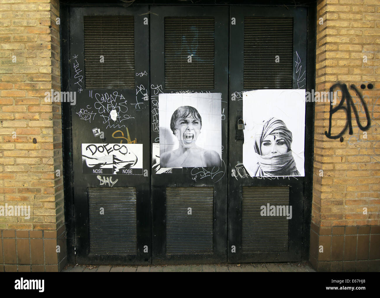 In bianco e nero poster di donne mescolati con graffiti su porte in una strada posteriore. Foto Stock
