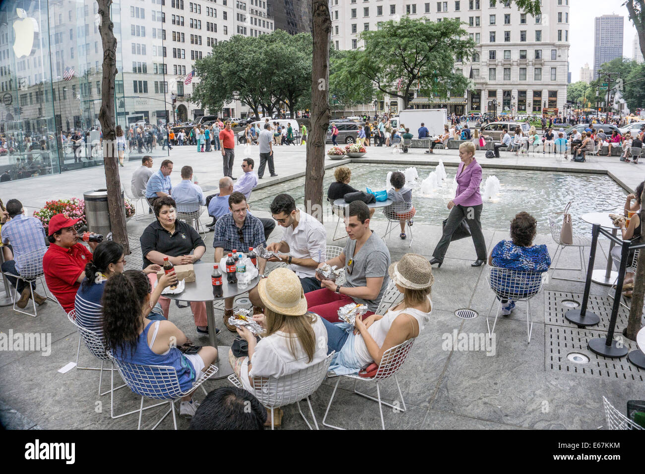 Gruppo seduti a tavola rotonda di socializzazione asporto mangiare il pranzo & Bere bicchieri di Coca Cola su plaza tra persone assiepati in midtown Manhattan Foto Stock