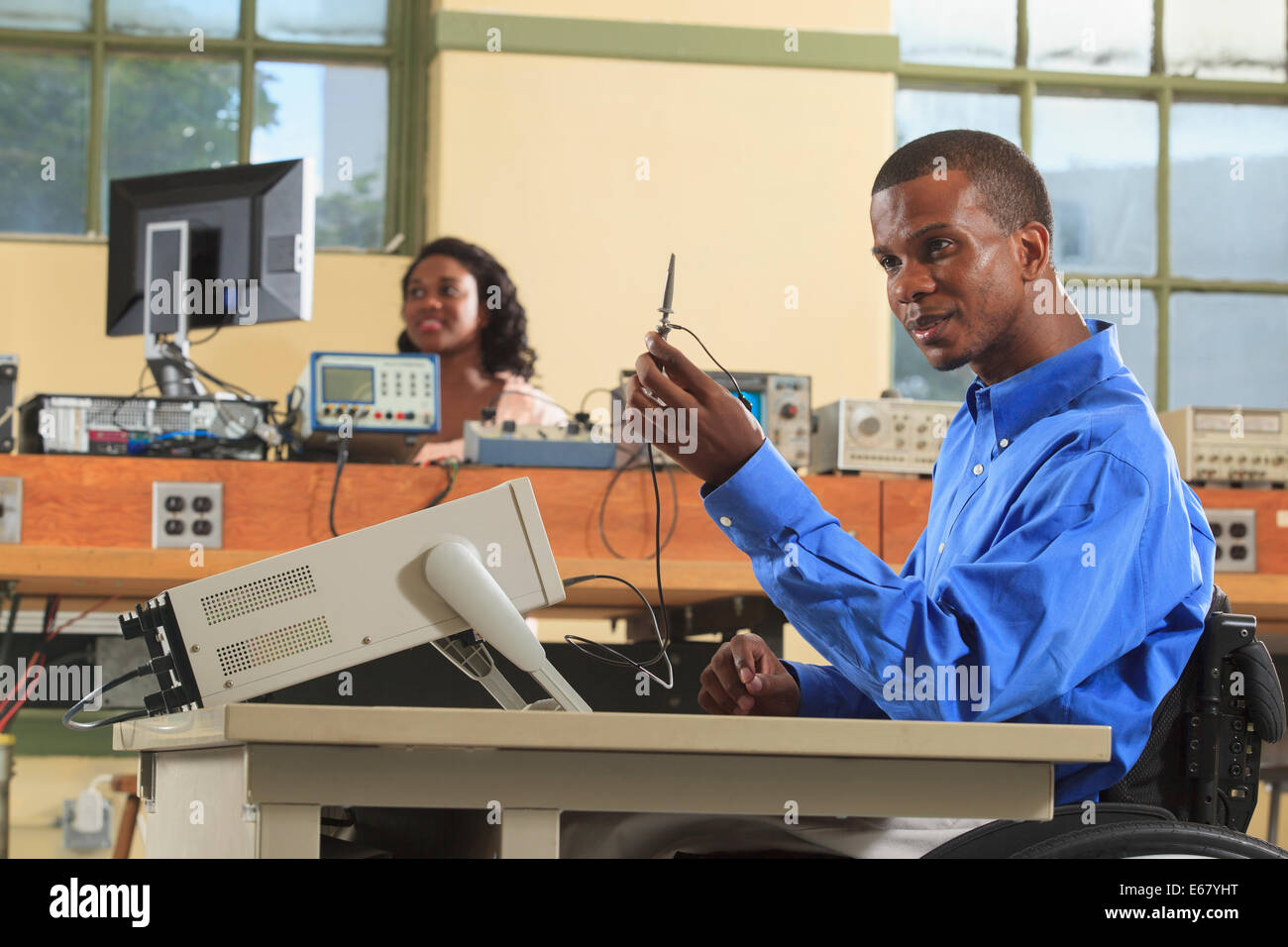 Gli studenti di ingegneria in un aula di elettronica, uno in una sedia a rotelle esaminando una sonda per oscilloscopio Foto Stock