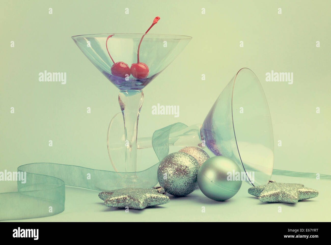 Lo spirito di festa blue martini cocktail con occhiali rossi ciliegie al maraschino e baubles di natale su un aqua sfondo blu. Foto Stock