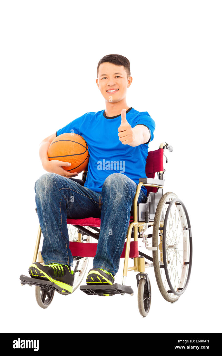 Asia giovane uomo seduto su una sedia a rotelle e il pollice in su con una palla da basket Foto Stock