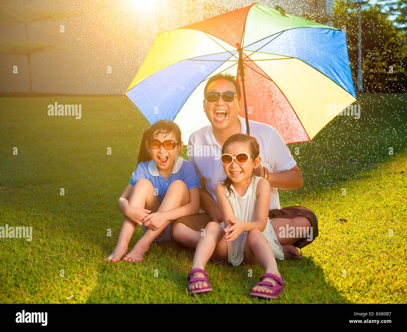 Padre e figlie seduto su un prato con ombrello coloratissimo Foto Stock