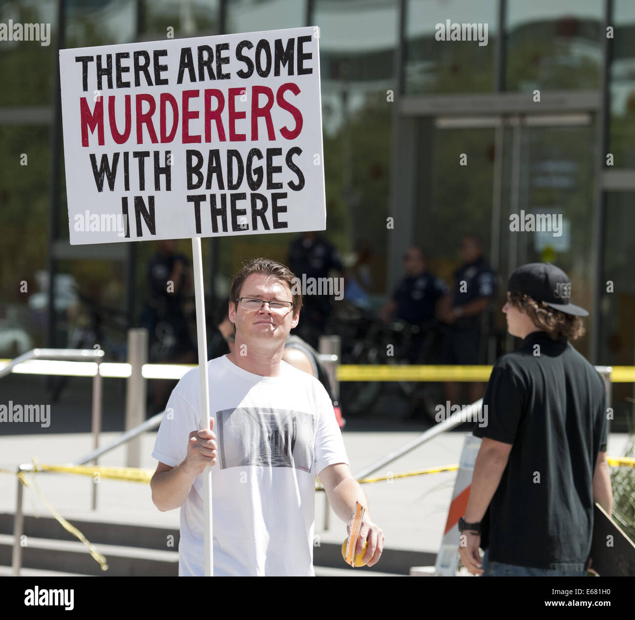 Los Angeles, California, USA. 17 Ago, 2014. Un uomo cammina passato LAPD Sede centrale con un segno di protesta come LAPD ufficiali stand in posizione dietro una linea di polizia domenica pomeriggio.--------circa 800 manifestanti radunati davanti alla Los Angeles il dipartimento di polizia nel centro cittadino di domenica pomeriggio per protestare contro il funzionario coinvolte le riprese di un Ezell Ford in South Central Los Angeles la scorsa settimana nonché per mostrare il loro sostegno per i residenti di Ferguson, Missouri, nelle loro manifestazioni di protesta contro la polizia vi. La folla visualizzati cartelloni e cartelli con slogan contro la polizia, unendo assieme a Foto Stock