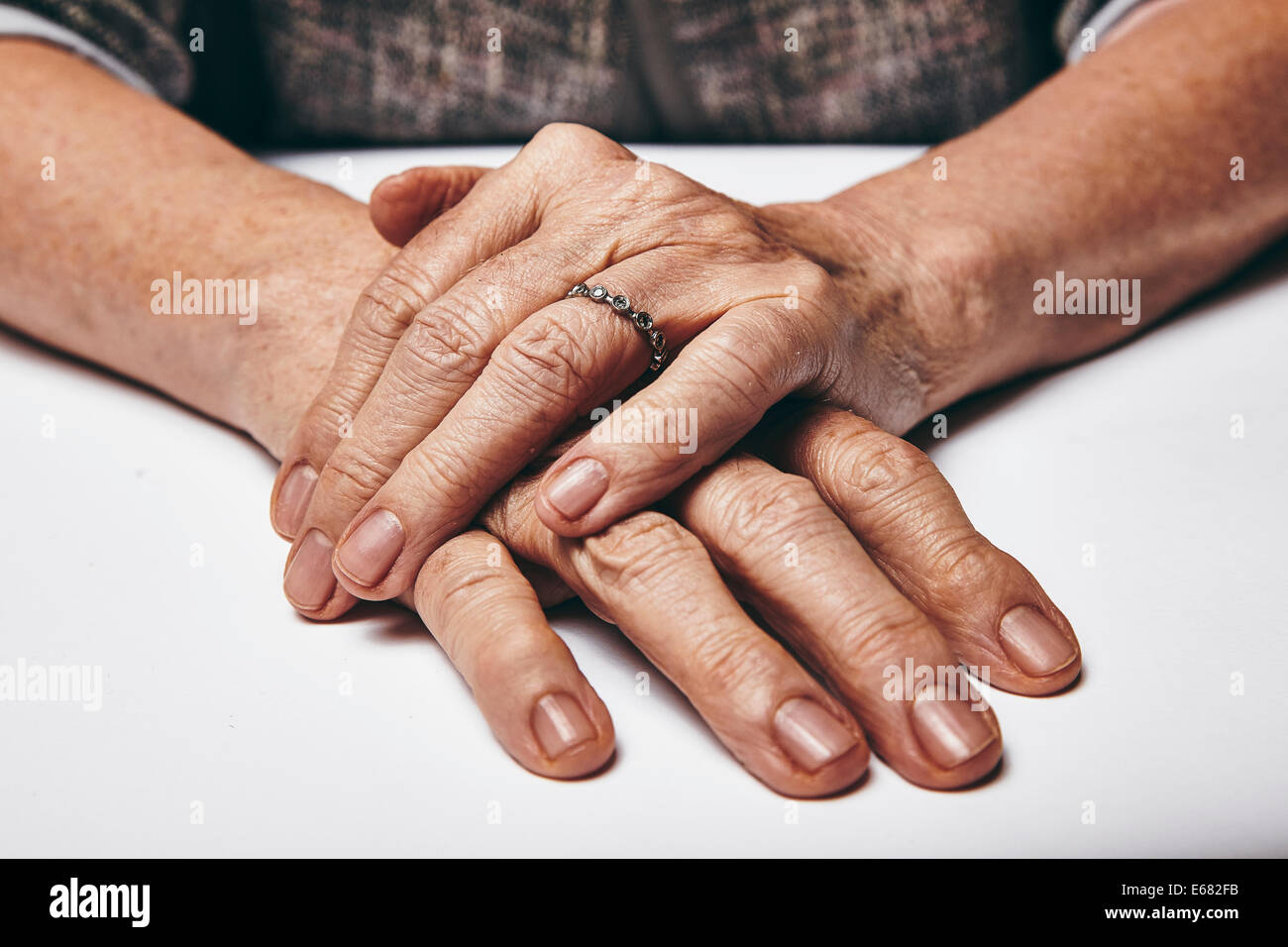 Macro di una vecchia signora seduta con le mani giunte su un tavolo. Donna anziana con le mani un anello di appoggio sulla superficie grigia. Foto Stock