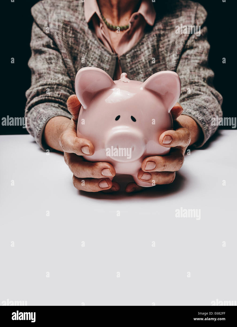 Ritagliato studio shot di senior mani femminili in possesso di una moneta banca seduti ad un tavolo. Vecchia donna tenendo un piggybank. Foto Stock