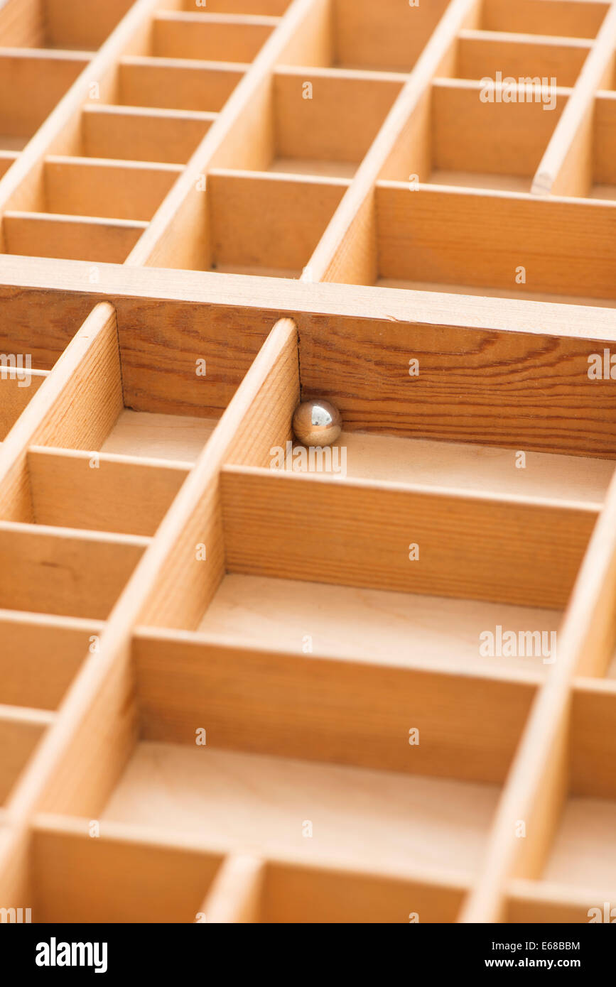 Piccola sfera di acciaio nella scatola di legno con scomparti vuoti. Immagine concettuale di solitudine, di solitudine e di rimanere intrappolati. Foto Stock