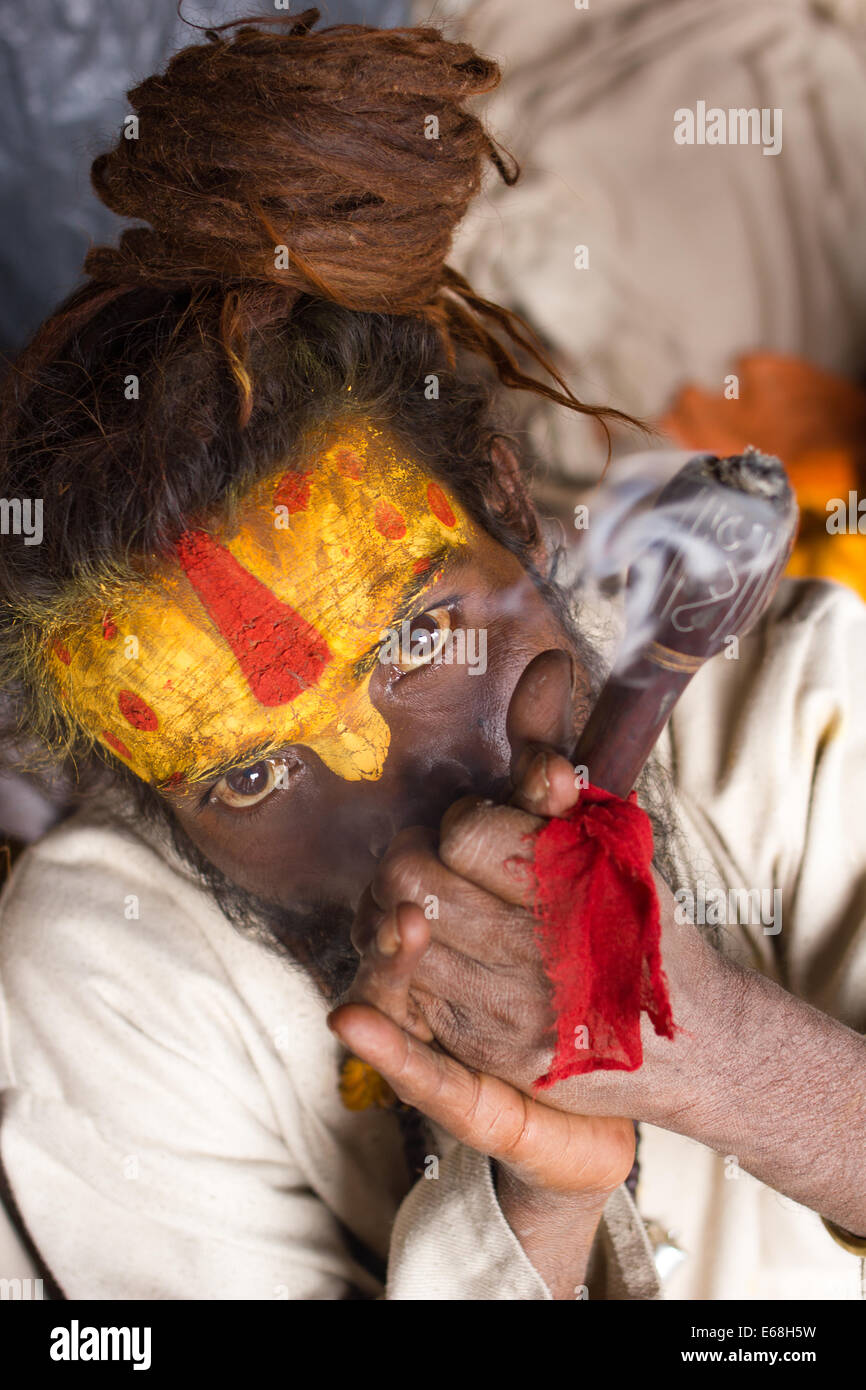 Un colorato sadhu indù (uomo santo) fumare una tubazione di hash al Tempio Hindu di Pashupatinath, Kathmandu, Nepal. Foto Stock