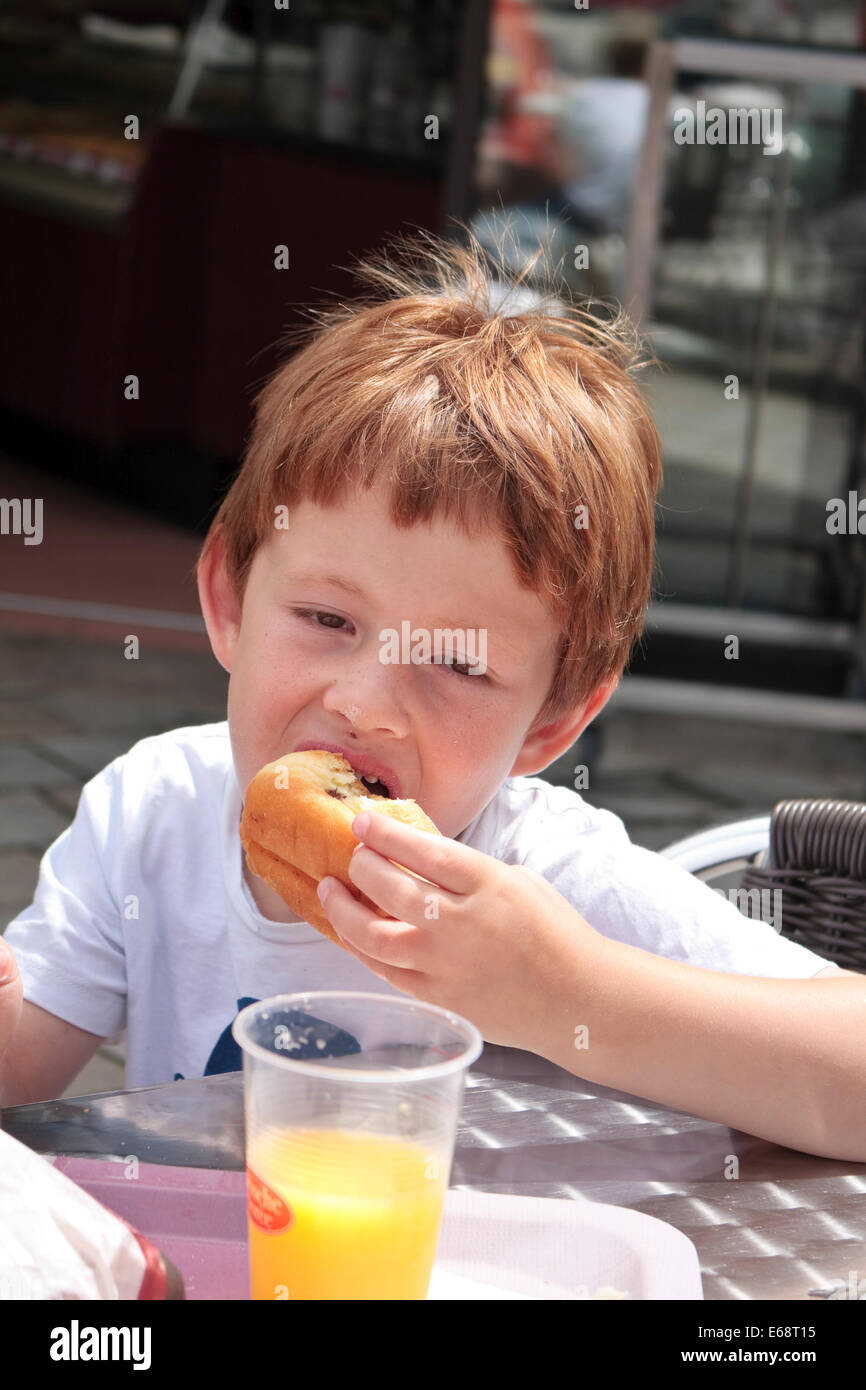 Un bambino di cinque anni, ragazzo di mangiare una ciambella a La Brioche Doree, Francia Foto Stock