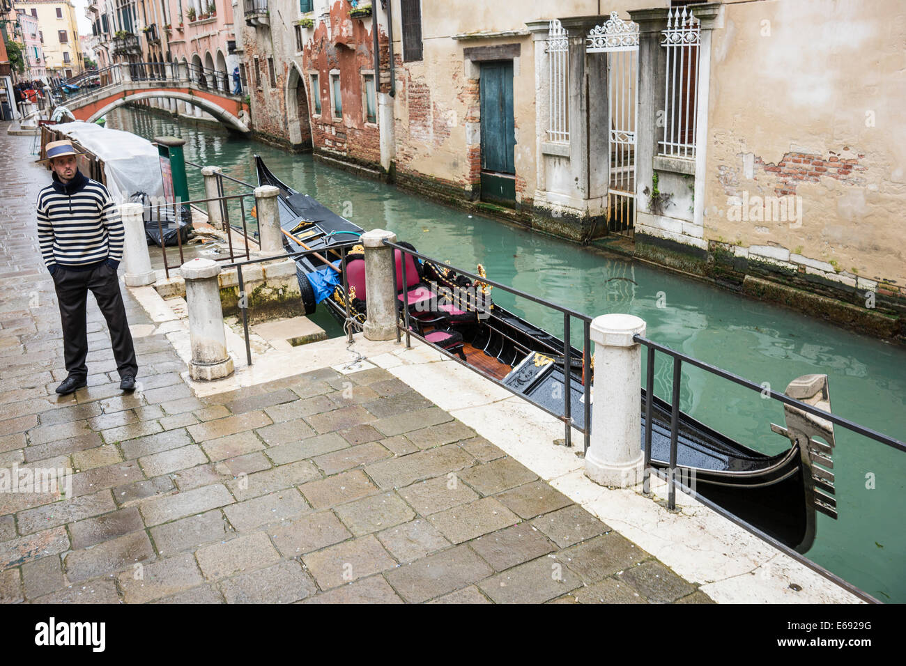 Gondoliere attende dal suo gondola per una tariffa su un canale laterale di Venezia. Foto Stock