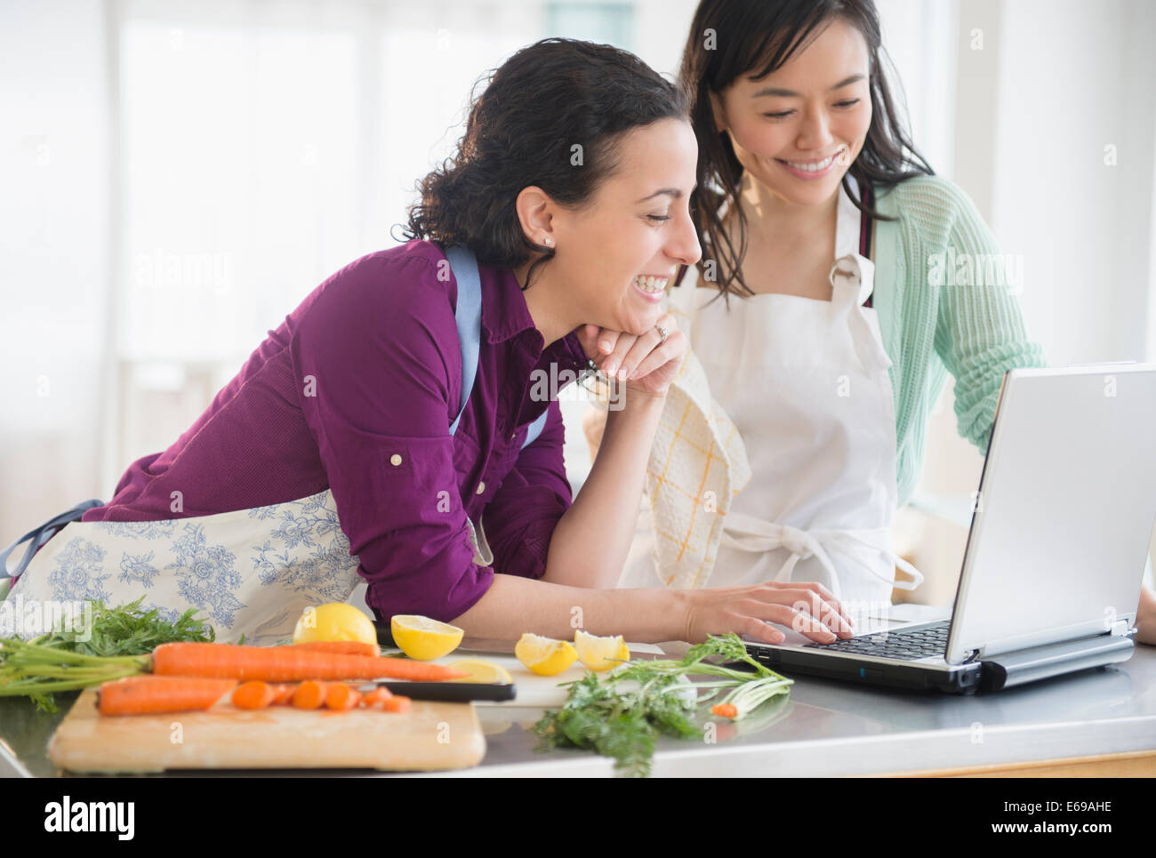 Le donne che usano i laptop e cucinare insieme Foto Stock