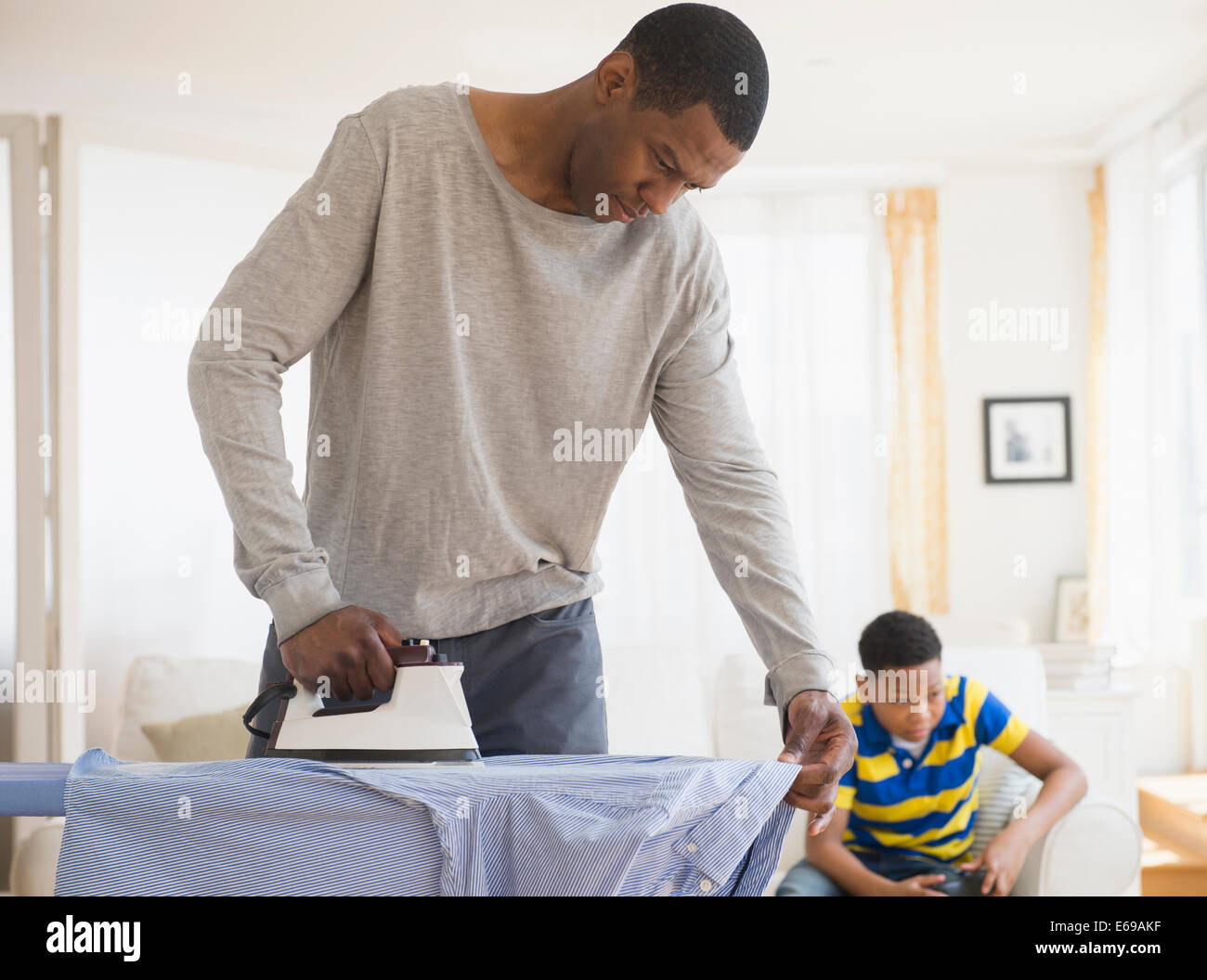 Padre la stiratura camicia mentre il figlio gioca giochi video Foto Stock
