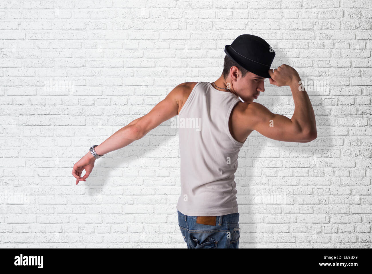 Hip giovane uomo che indossa un cappello a ballare, bianco contro un muro di mattoni Foto Stock