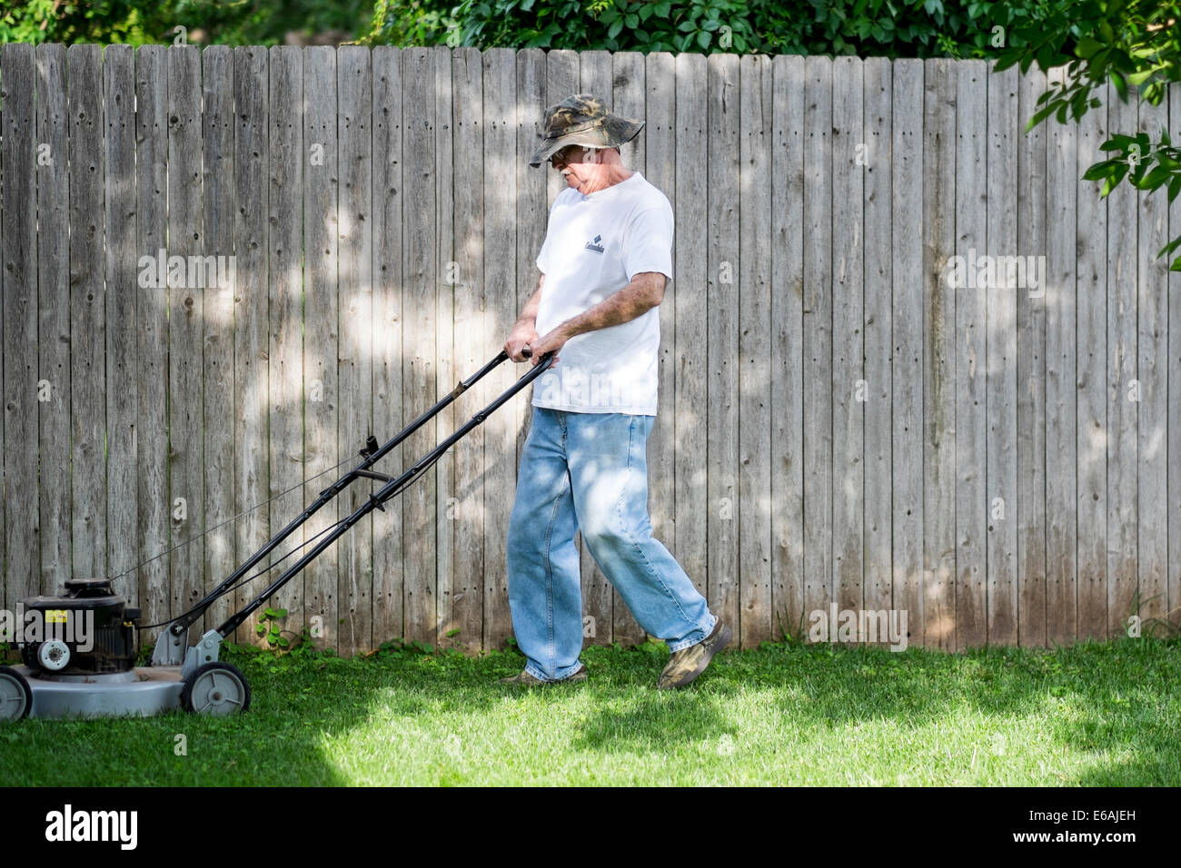Un anziano uomo che indossa un cappello mows il suo prato in pezzata sole e ombra in Oklahoma, Stati Uniti d'America Foto Stock