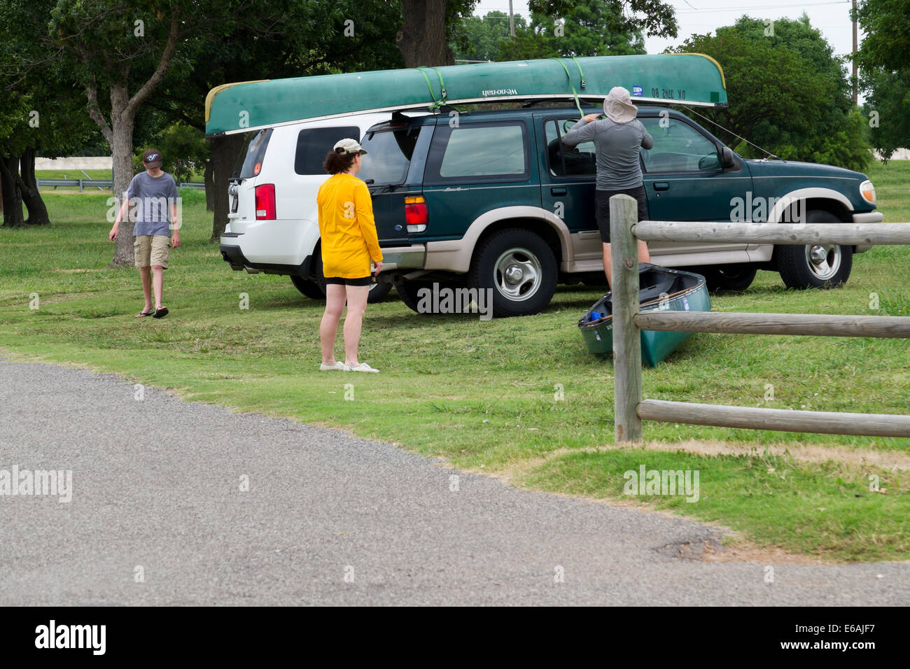 Un uomo fissa una canoa sulla sommità del suo veicolo in un lago di Oklahoma mentre due membri della famiglia sono nelle vicinanze. Oklahoma, Stati Uniti d'America. Foto Stock