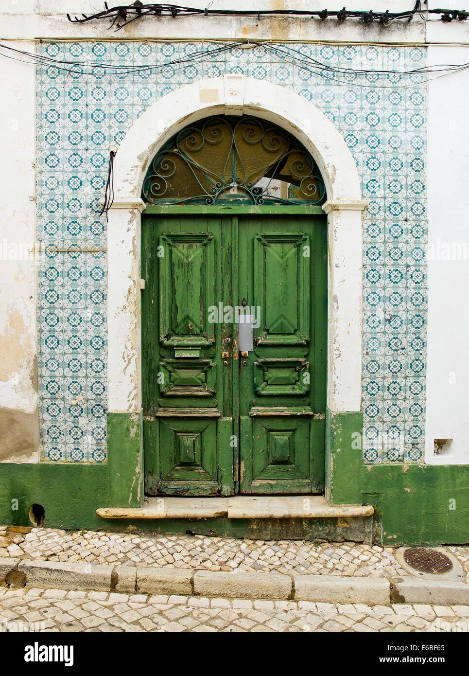 Il verde antico porta di legno in una casa con usurati parete piastrellata. Foto Stock