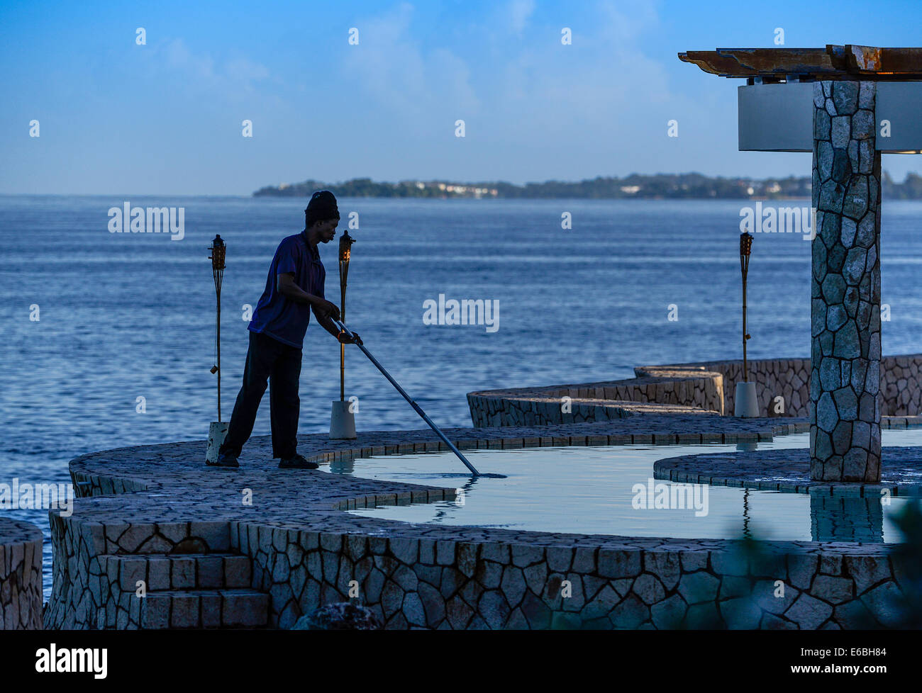 L'uomo pulisce resort piscina fronte oceano, Negril, Giamaica Foto Stock