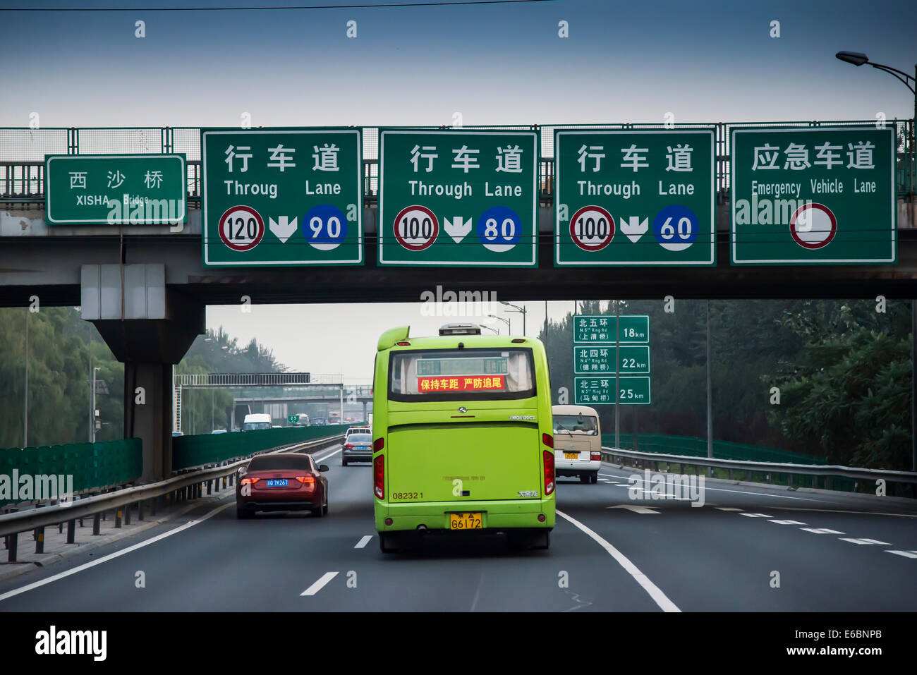 Il bus che viaggiano su 3-lane motorway con segni e un ponte a Pechino, Cina Foto Stock