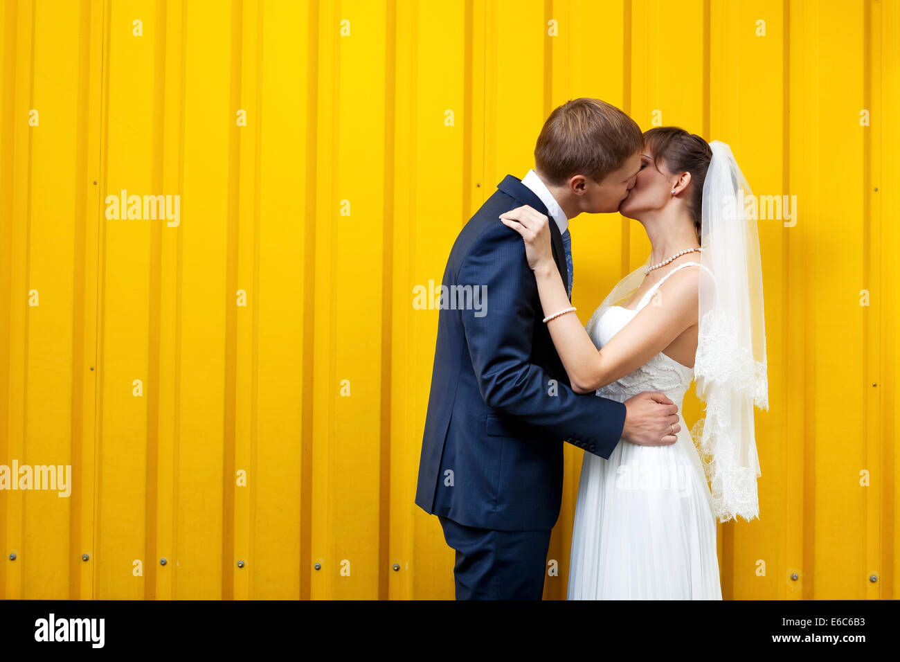Sposa e lo sposo baciare contro la parete gialla Foto Stock