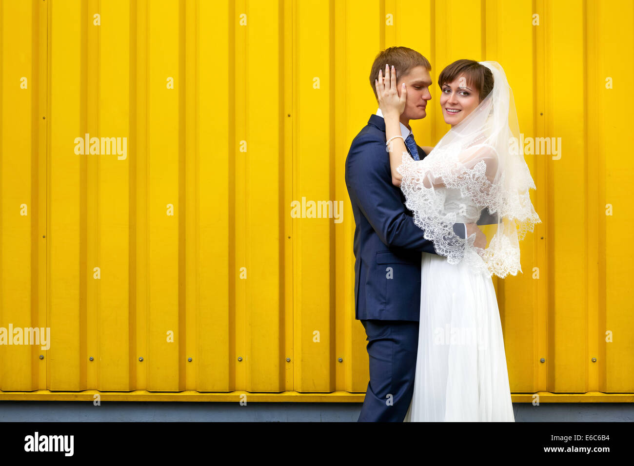 Sposa e lo sposo abbracciando contro la parete gialla Foto Stock
