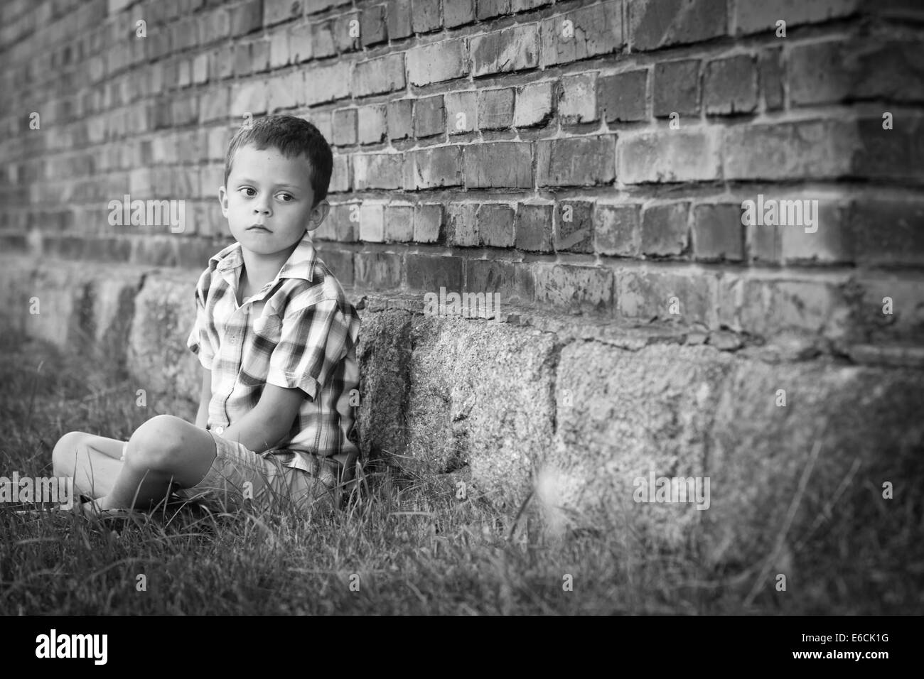 Immagine in bianco e nero del ragazzo seduto in erba a parete Foto Stock