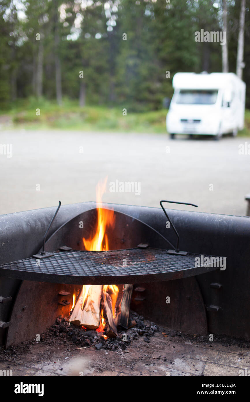 Accogliente fuoco di campo con il campeggio auto in background. Camping car è al di fuori della messa a fuoco. Foto Stock