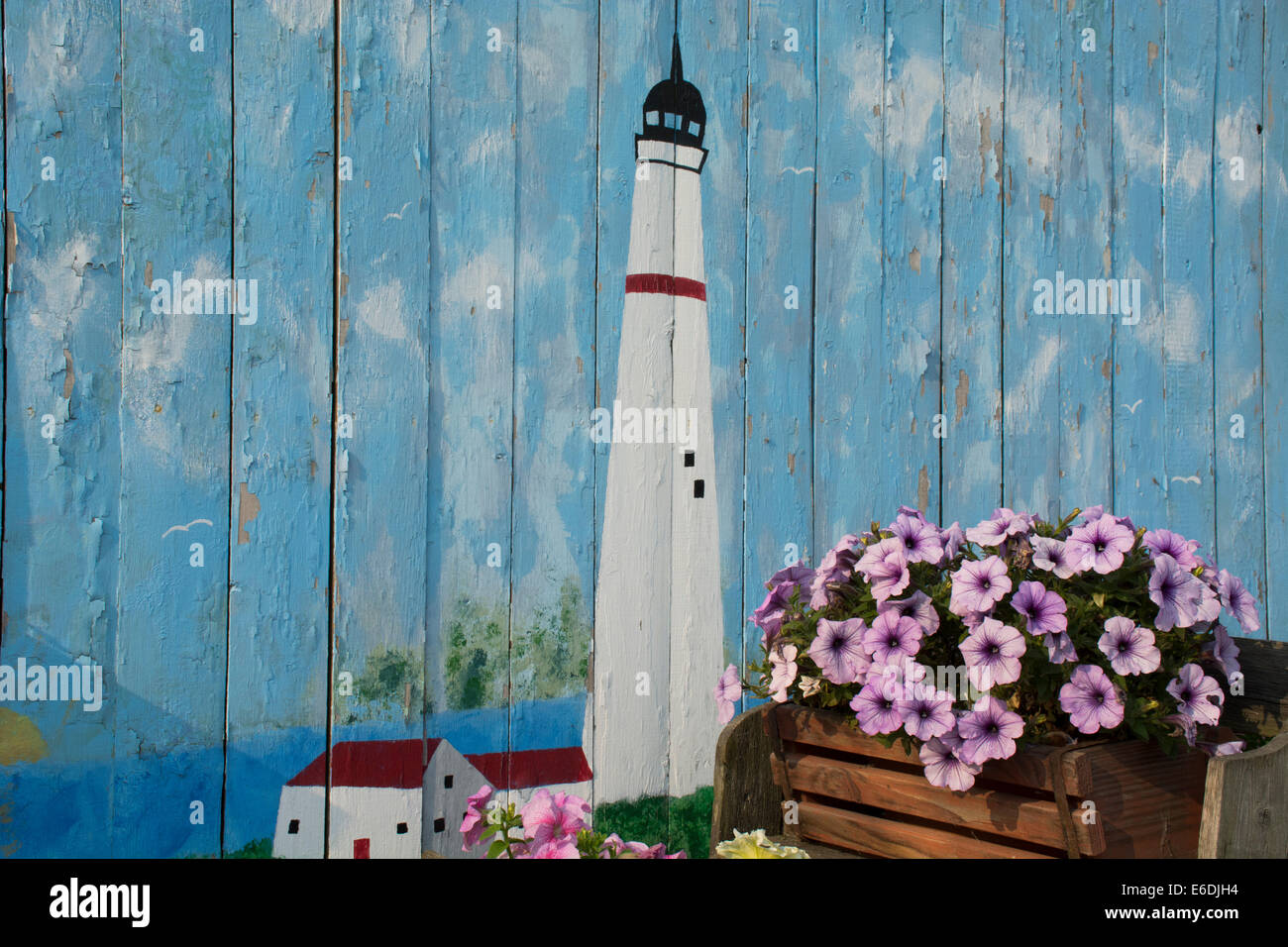 Michigan, San Ignace. Carro antico riempito di fiori nella parte anteriore di un dipinto di parete in legno con il faro. Foto Stock