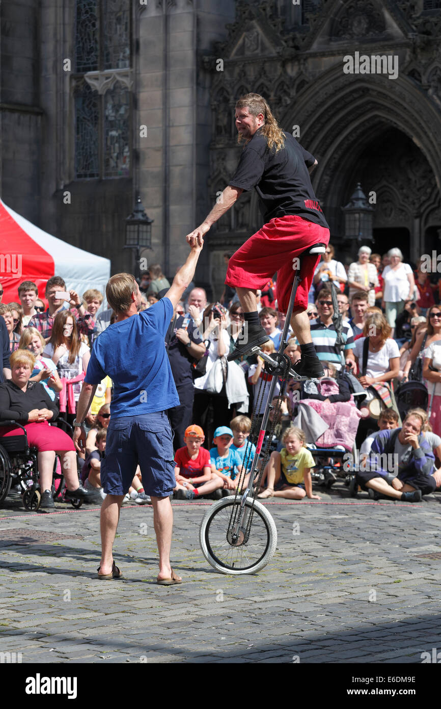 Street Performer Mullet Man in un monociclo con un volontario durante l'Edinburgh Festival Fringe, Scozia, Regno Unito Foto Stock