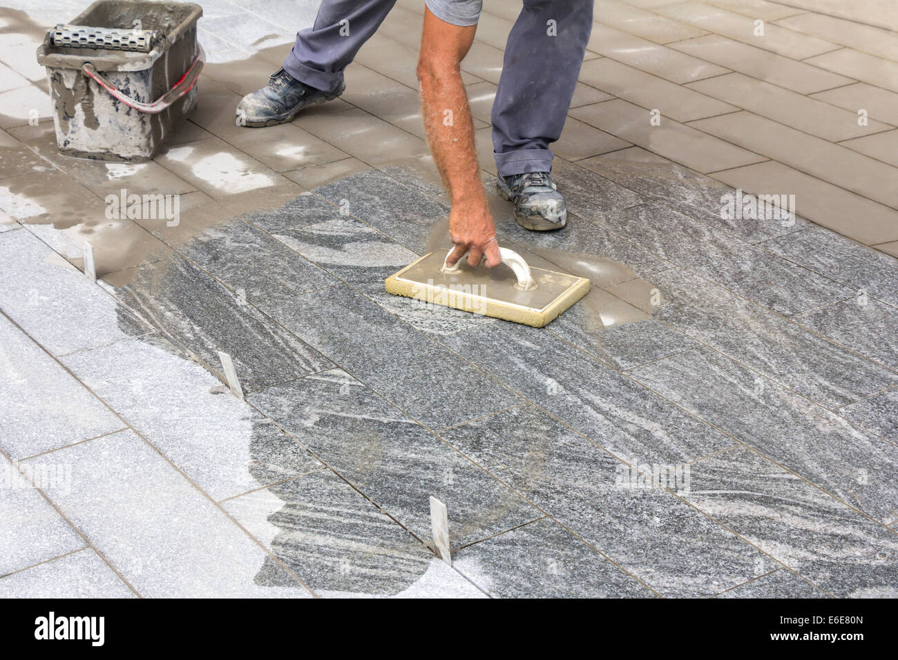 Lavoratore riempitivi di fughe di piastrelle con frattazzo in gomma grigia e malta di cemento Foto Stock