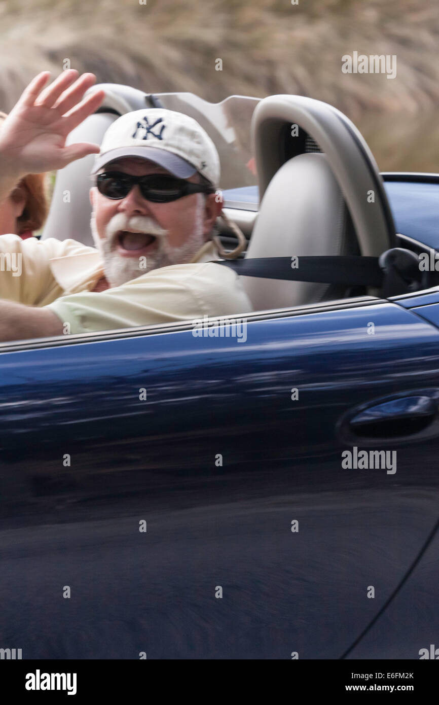 Coppia in pensione con uomo felice sventolando la guida trasgressivi Porsche Boxster, FL, Stati Uniti d'America Foto Stock