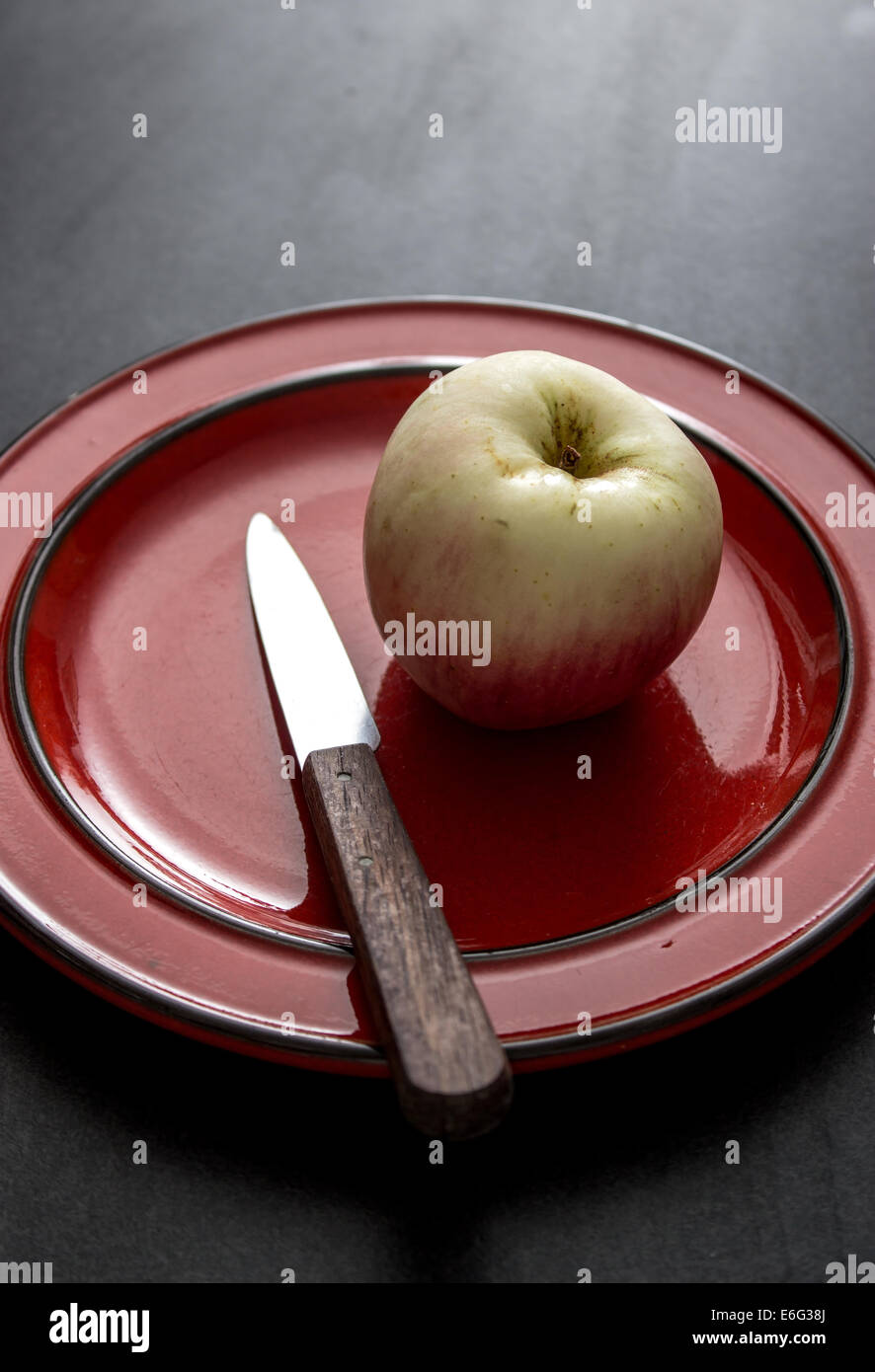 Unico di rosso e di giallo apple si siede su una piastra con un coltello,al buio su un tavolo rustico,fuoco selettivo. Foto Stock