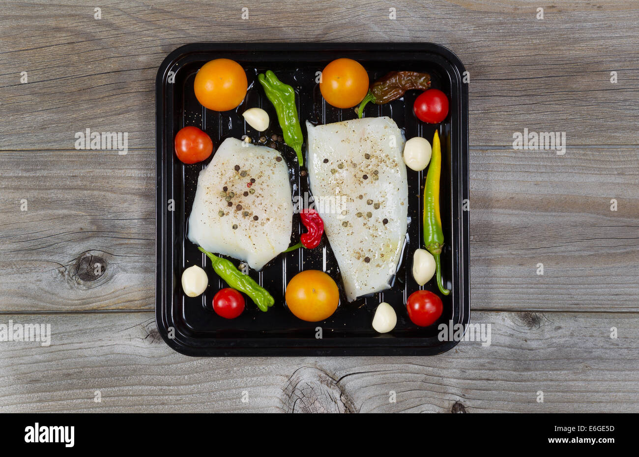 Vista superiore del crudo fresco Cod i filetti di pesce nel recipiente di cottura con pomodori, aglio, peperoncino e sale di peppe su rustiche tavole in legno Foto Stock