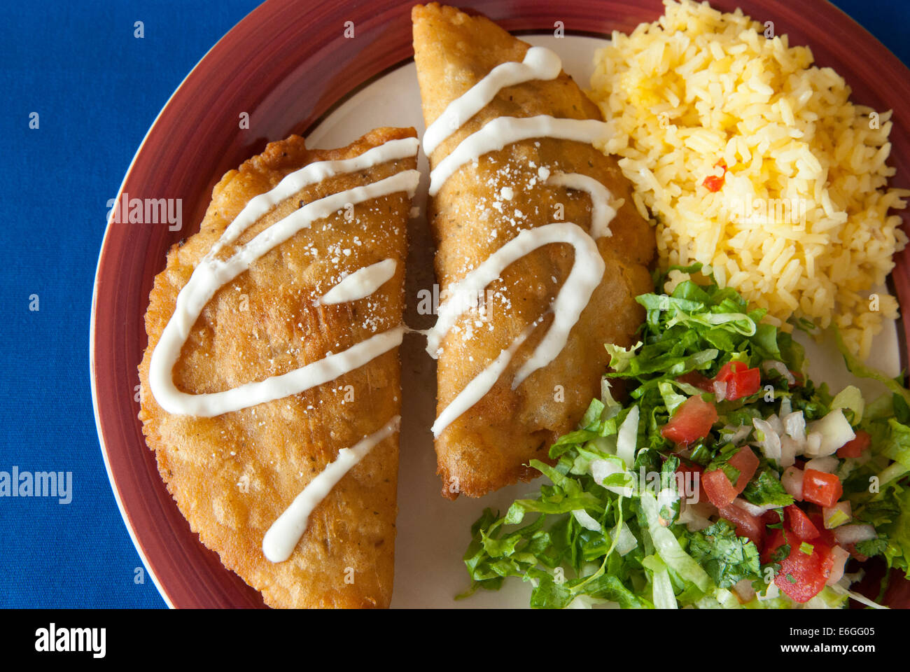 Oltre il colpo alla testa di empanada con riso allo zafferano e insalata su una tovaglia blu Foto Stock