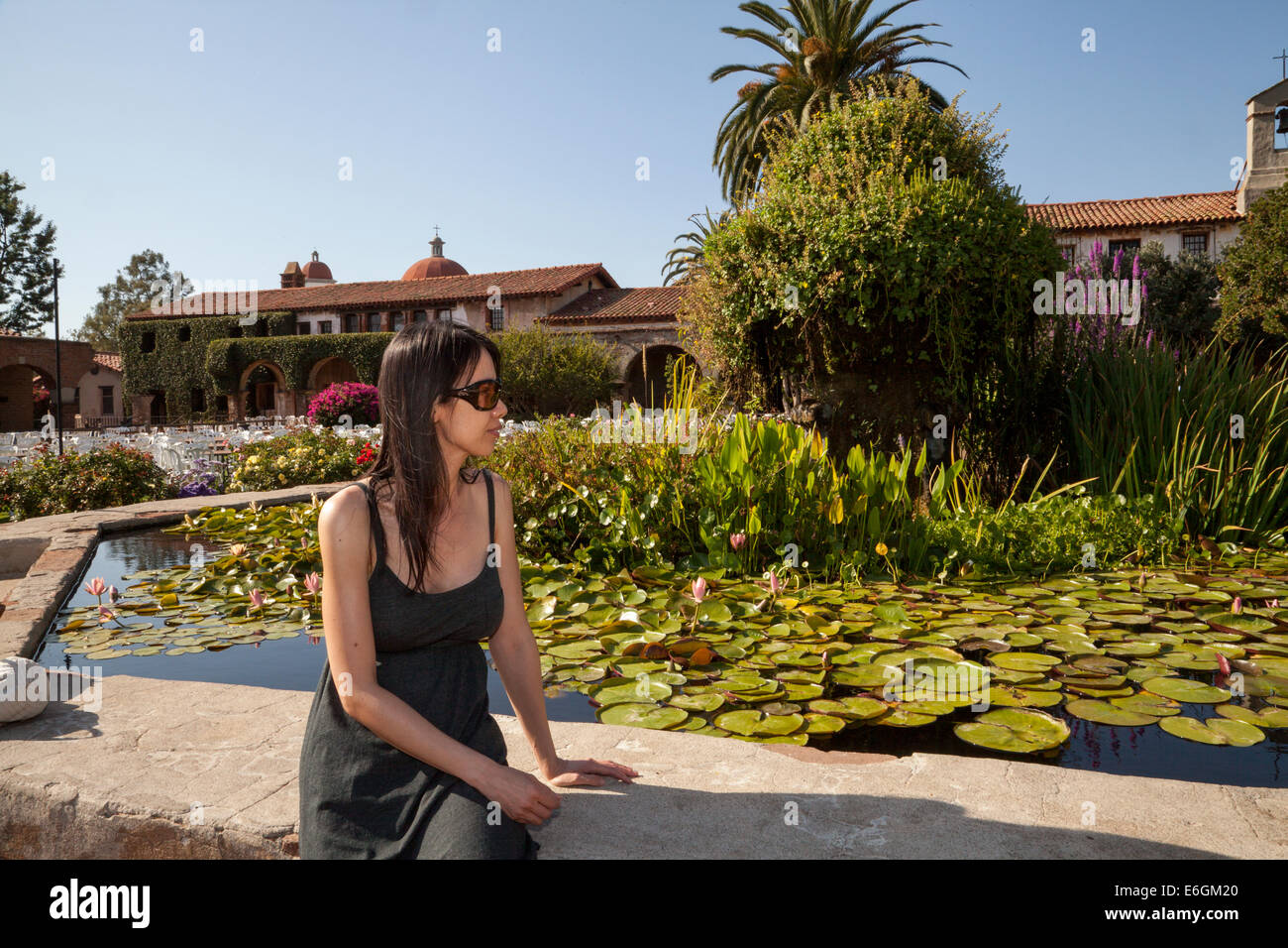Asia femmina seduto da lily pond nel cortile centrale della Missione di San Juan Capistrano, CALIFORNIA, STATI UNITI D'AMERICA Foto Stock