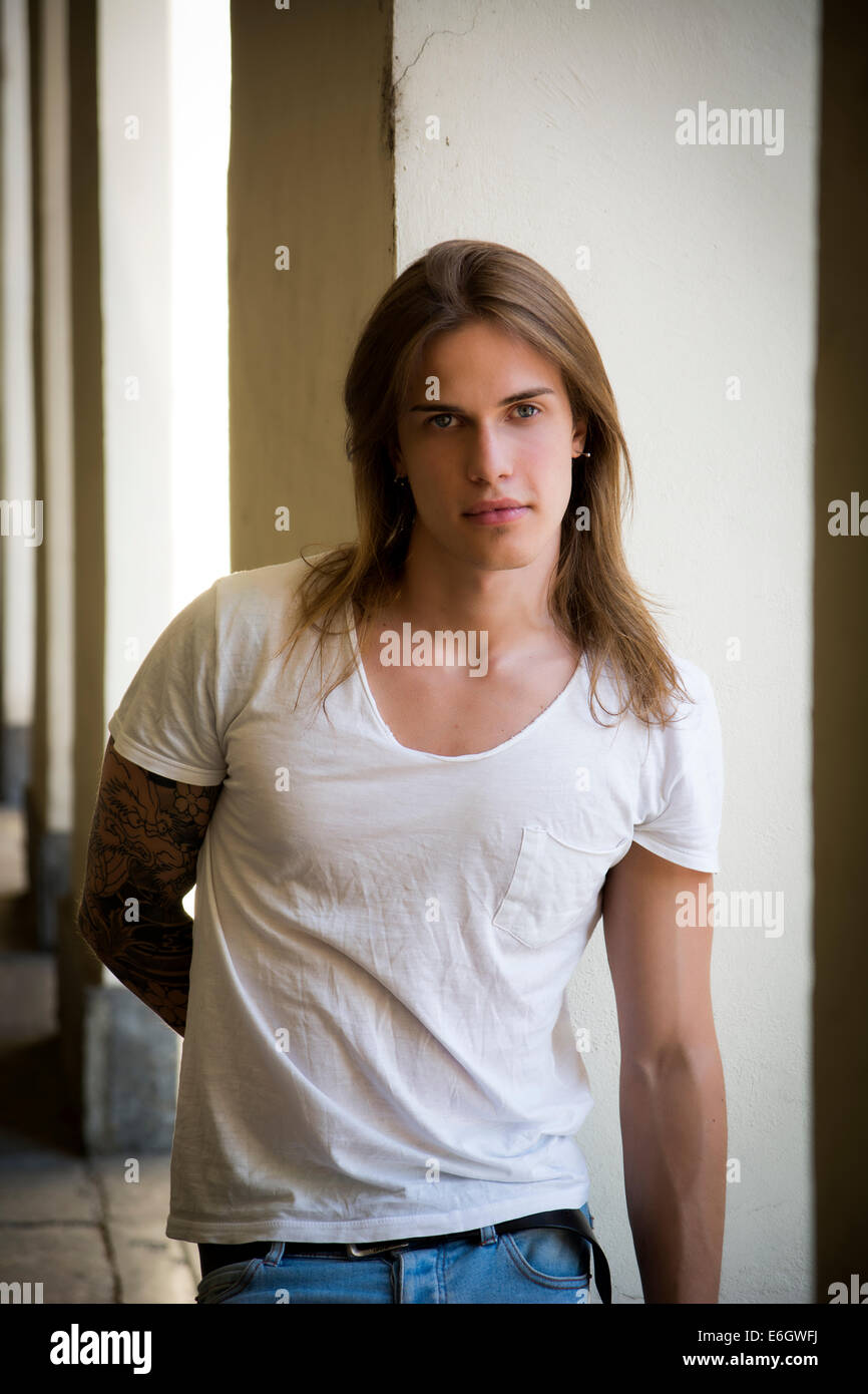 Bello capelli lunghi Uomo in camicia bianca in piedi oltre al corridoio Foto Stock