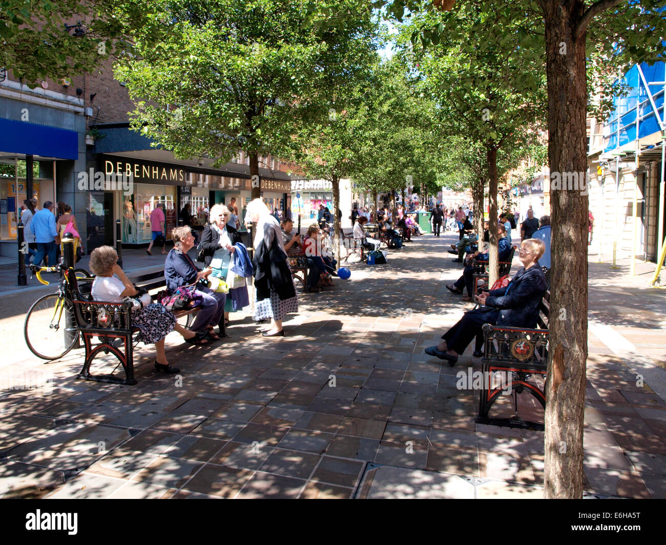 Gli amanti dello shopping in appoggio sulle panchine pubbliche nell'ombra di un albero in una calda giornata estiva, Worcester City Centre, Regno Unito Foto Stock