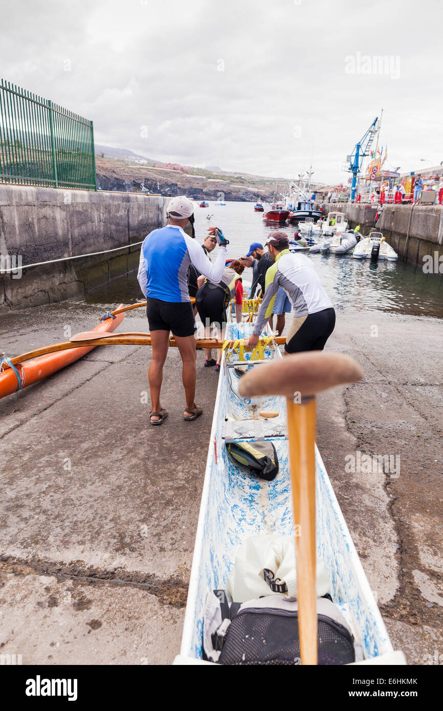 Sei uomo squadra di canottaggio lanciando una canoa outrigger at Playa San Juan, Tenerife, Isole Canarie, Spagna. Foto Stock