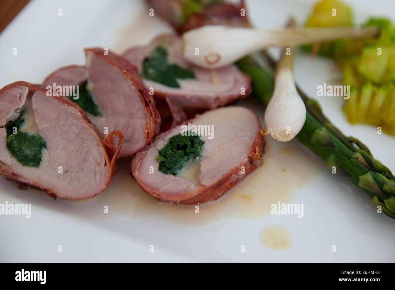 Filetto alla griglia di carne di maiale con ripieno di formaggio e spinaci rivestita con pancetta. Piatto di lato grigliate di giovani cipolla, gli asparagi e le zucchine. Foto Stock