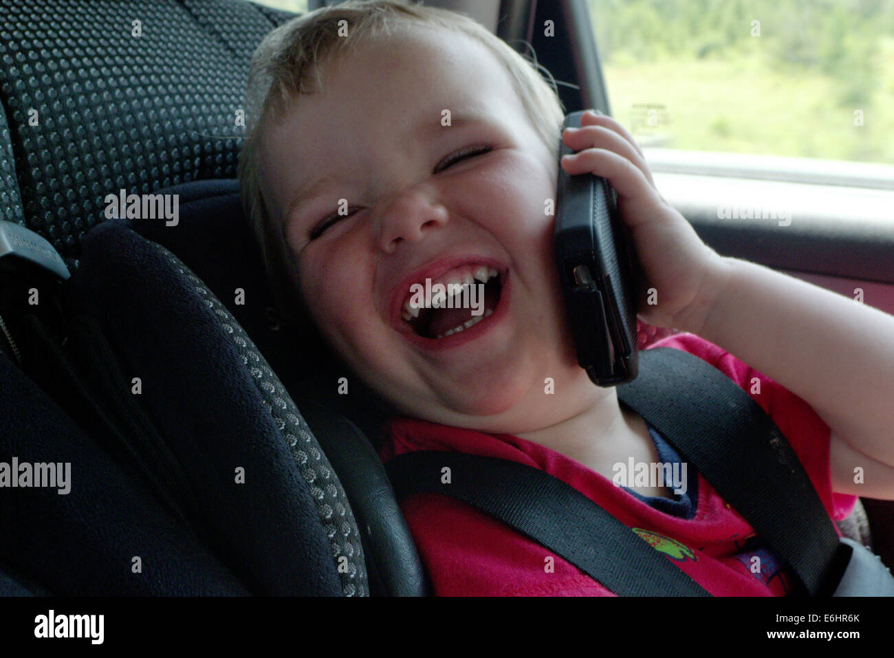 Un bambino nel sedile di un'auto di ridere fingendo di utilizzare un iphone Foto Stock