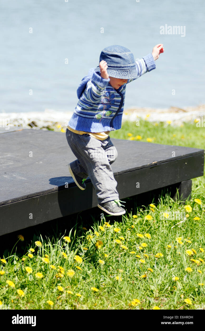 Un giovane ragazzo che salta da una piattaforma di legno Foto Stock