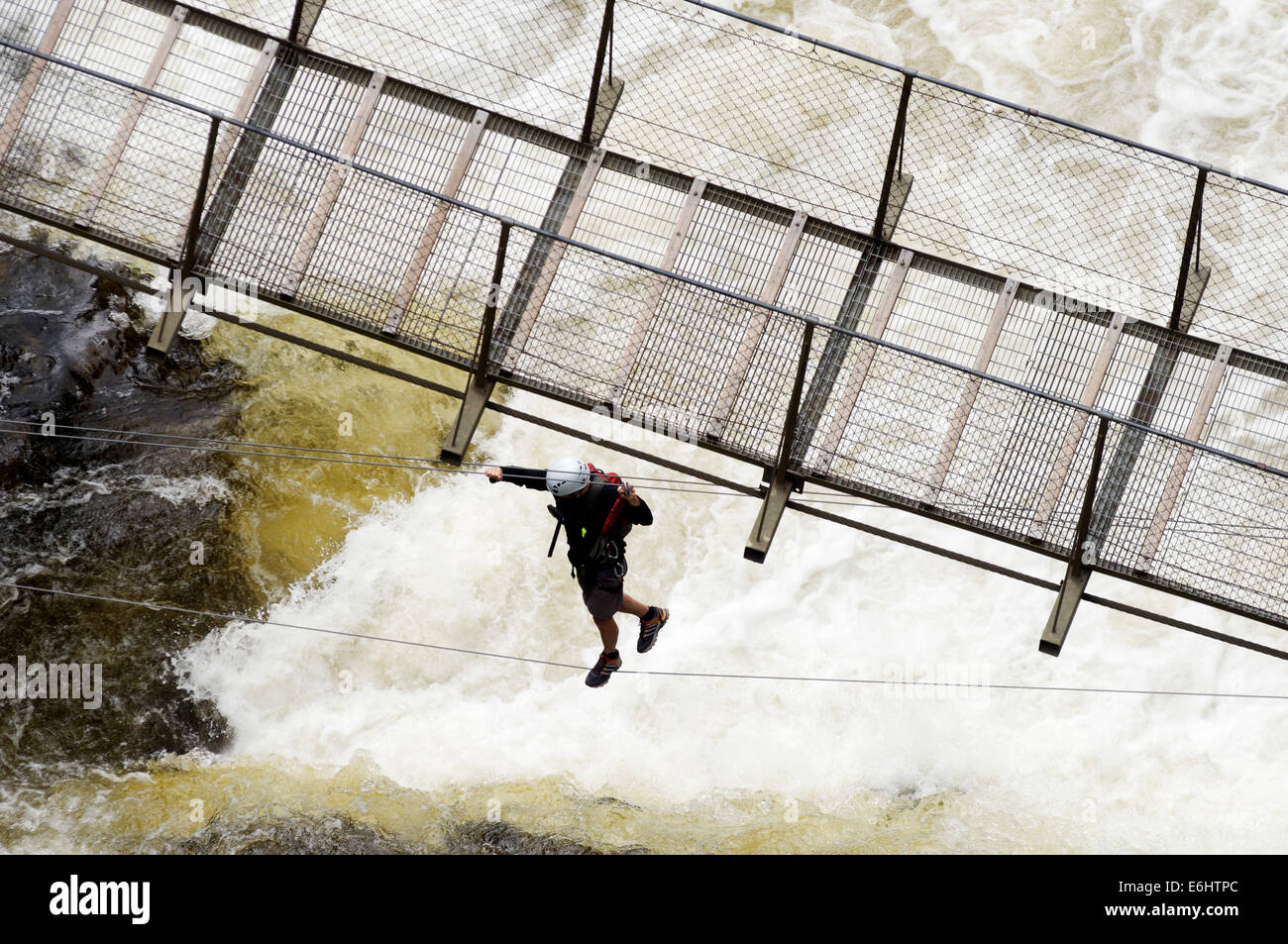 Un uomo che attraversa un fiume turbolento su un ponticello in Canyon Ste Anne in Quebec, Canada Foto Stock