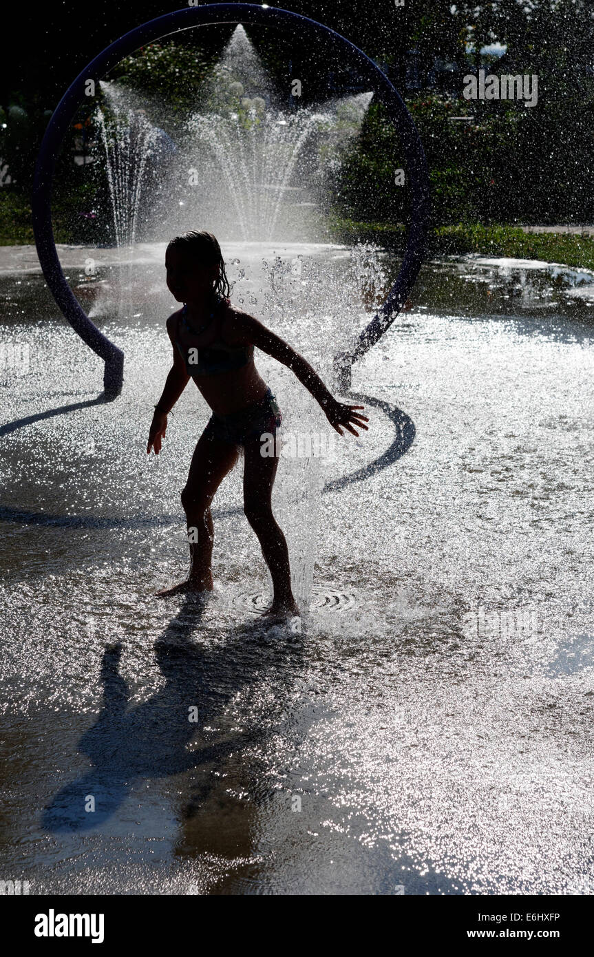 Una giovane ragazza che gioca in acqua delle fontane in una calda giornata estiva Foto Stock
