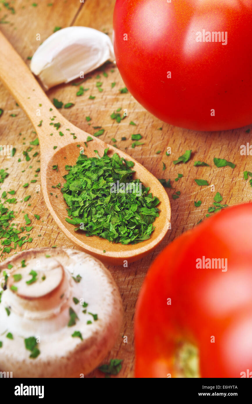 Prezzemolo tritato sul cucchiaio di legno in cucina. Preparazione alimentare dello sfondo. Foto Stock
